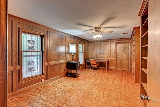 home office featuring ceiling fan, crown molding, wooden walls, and a textured ceiling