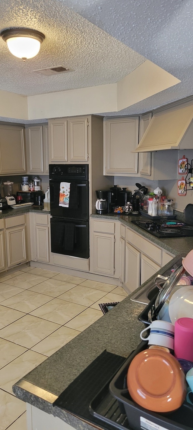 kitchen featuring black appliances, premium range hood, light tile patterned floors, and a textured ceiling