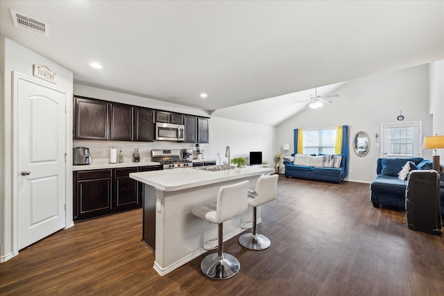 kitchen featuring sink, a center island with sink, dark wood-type flooring, appliances with stainless steel finishes, and a kitchen breakfast bar