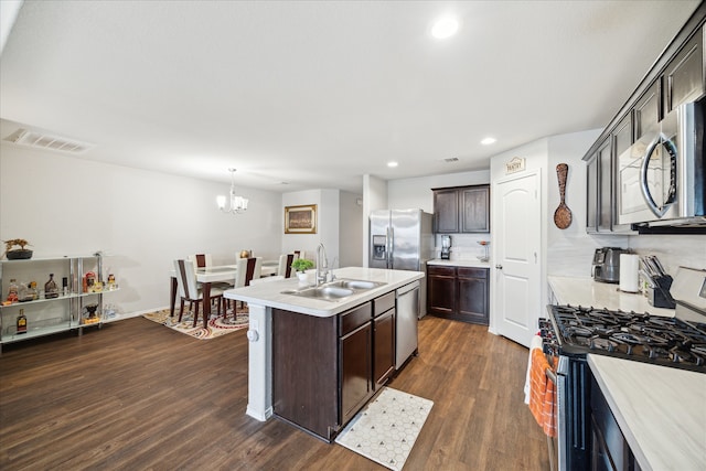 kitchen with appliances with stainless steel finishes, dark wood-type flooring, an island with sink, decorative light fixtures, and dark brown cabinetry