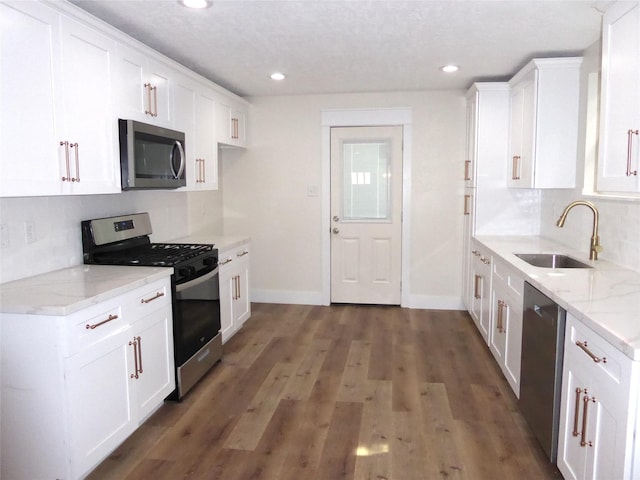 kitchen with white cabinets, sink, light stone counters, appliances with stainless steel finishes, and dark hardwood / wood-style flooring