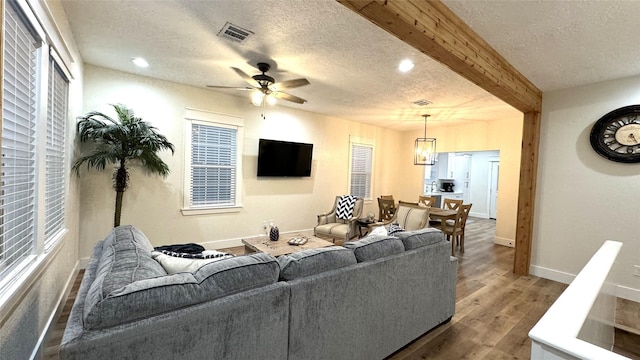 living room with ceiling fan with notable chandelier, beam ceiling, wood-type flooring, and a textured ceiling