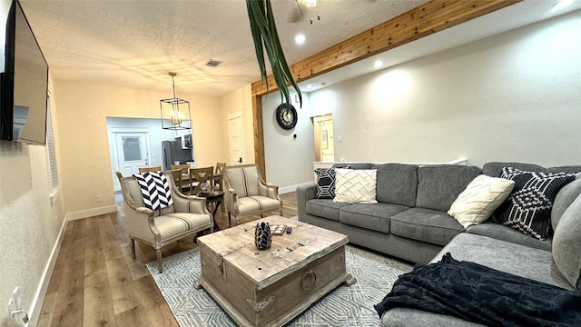 living room with beamed ceiling, wood-type flooring, a textured ceiling, and an inviting chandelier