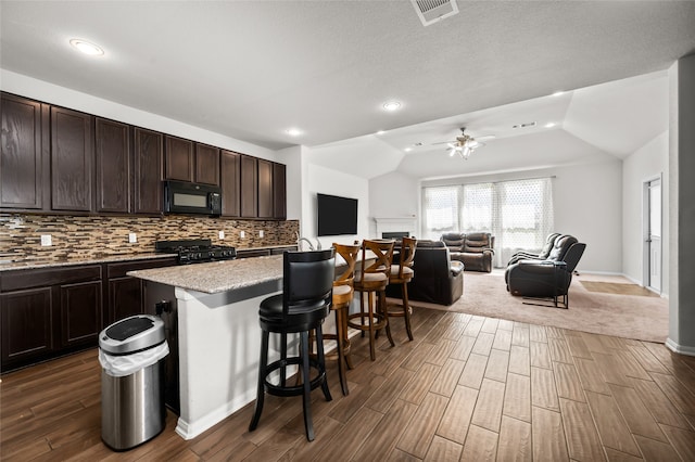 kitchen with dark hardwood / wood-style floors, black appliances, a breakfast bar, a center island, and ceiling fan