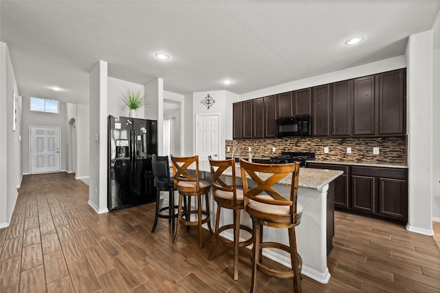 kitchen with an island with sink, black appliances, a kitchen breakfast bar, and dark wood-type flooring