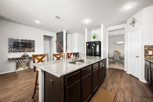 kitchen with a kitchen bar, dark hardwood / wood-style flooring, an island with sink, hanging light fixtures, and black fridge