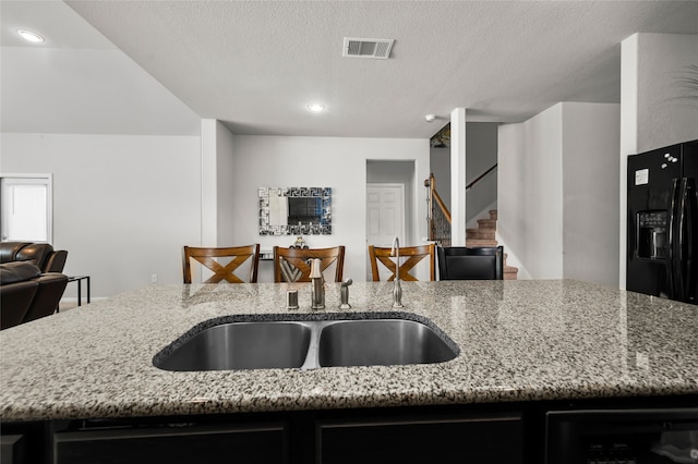 kitchen featuring a textured ceiling, light stone counters, and sink