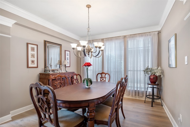 dining space with light wood-type flooring, ornamental molding, and an inviting chandelier