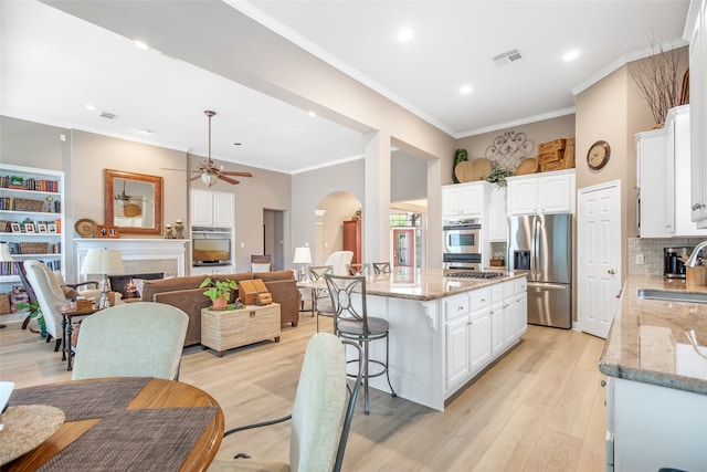 kitchen featuring an island with sink, ceiling fan, light stone countertops, and appliances with stainless steel finishes