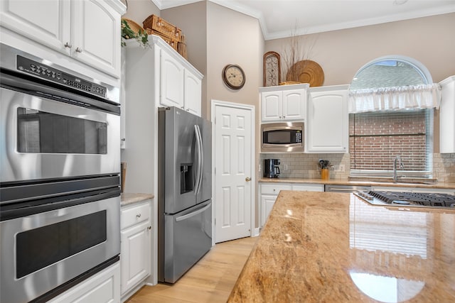 kitchen featuring ornamental molding, white cabinetry, backsplash, appliances with stainless steel finishes, and light hardwood / wood-style floors