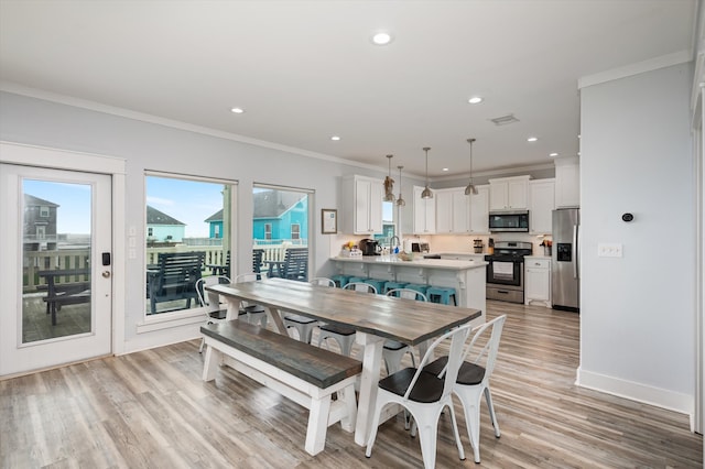 dining room with ornamental molding, light wood-type flooring, and a healthy amount of sunlight