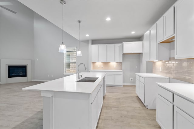 kitchen with light wood-type flooring, a kitchen island with sink, a sink, a glass covered fireplace, and white cabinets