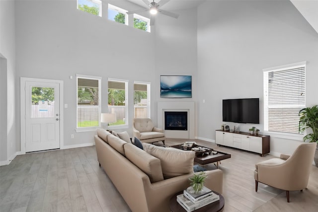 living area with wood finished floors, baseboards, a high ceiling, ceiling fan, and a glass covered fireplace