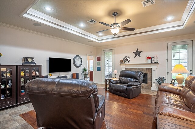 living room featuring ceiling fan, a tiled fireplace, a tray ceiling, and hardwood / wood-style flooring