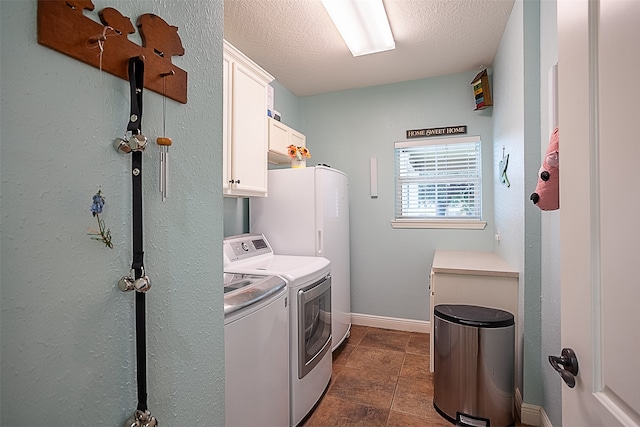 clothes washing area with separate washer and dryer, dark tile patterned floors, cabinets, and a textured ceiling