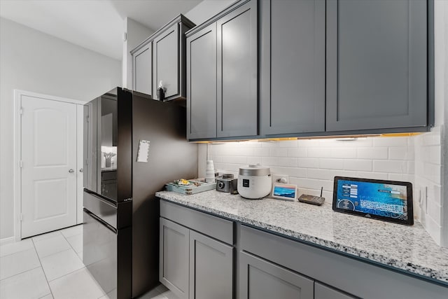 kitchen with gray cabinetry, light tile patterned floors, light stone countertops, and black refrigerator with ice dispenser