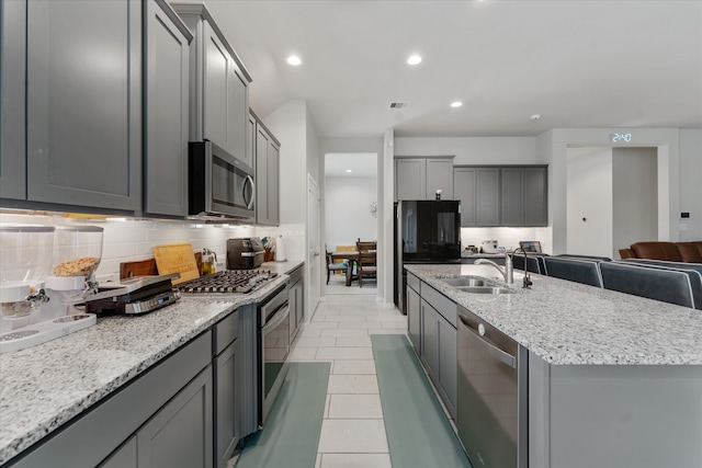 kitchen with appliances with stainless steel finishes, sink, gray cabinets, an island with sink, and decorative backsplash