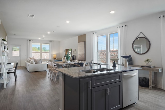 kitchen featuring a center island with sink, stone countertops, light hardwood / wood-style floors, stainless steel dishwasher, and sink