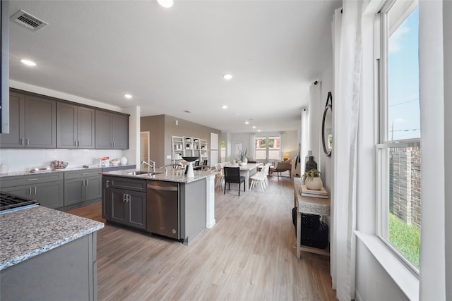 kitchen with a wealth of natural light, stainless steel dishwasher, light stone counters, and light hardwood / wood-style flooring