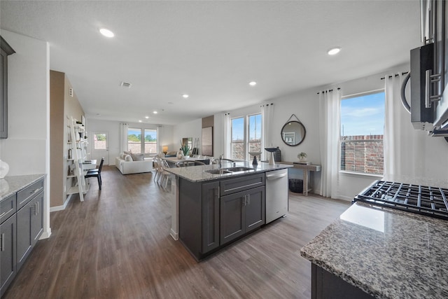 kitchen with appliances with stainless steel finishes, light stone countertops, dark hardwood / wood-style flooring, sink, and a center island with sink