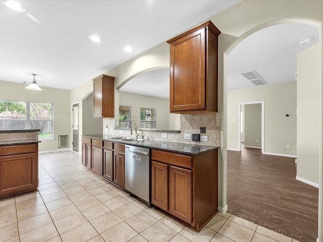 kitchen with sink, light hardwood / wood-style flooring, stainless steel dishwasher, backsplash, and dark stone counters