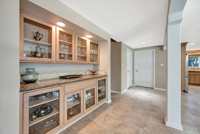 bar featuring stainless steel fridge and dark stone counters