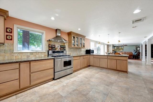 2601 Christopher Sq, Galveston, TX 77551 - kitchen with wall chimney exhaust hood, stainless steel appliances, light brown cabinetry, open floor plan, and glass insert cabinets