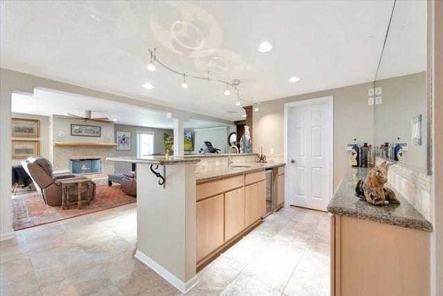 2601 Christopher Sq, Galveston, TX 77551 - kitchen featuring open floor plan, a peninsula, light stone countertops, a warm lit fireplace, and beverage cooler