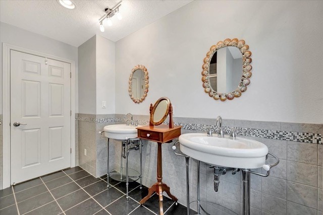 bathroom with tile patterned flooring, a textured ceiling, tile walls, and double sink