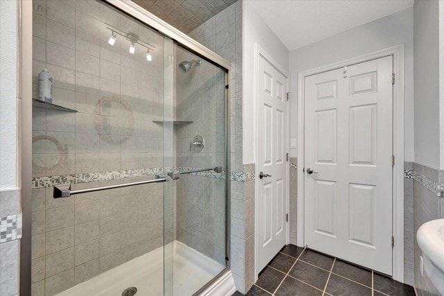 bathroom featuring tile patterned flooring, a shower with door, and tile walls