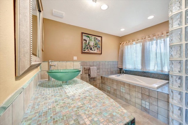 bathroom featuring tile patterned flooring, a relaxing tiled tub, and sink