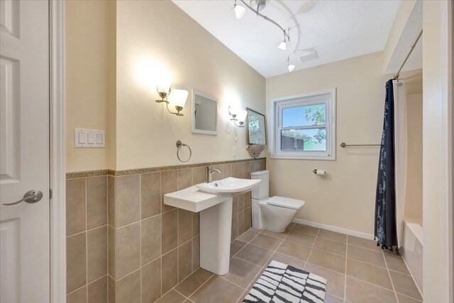 bathroom featuring tile patterned flooring, shower / bath combination with curtain, toilet, and tile walls