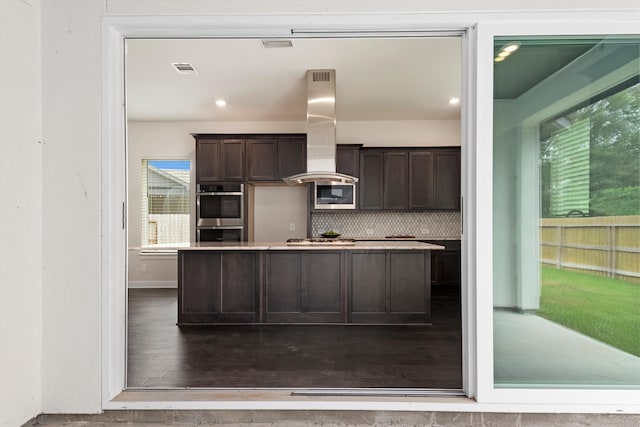 kitchen featuring hardwood / wood-style floors, appliances with stainless steel finishes, decorative backsplash, island range hood, and dark brown cabinetry