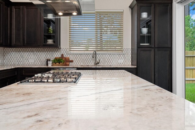 kitchen featuring backsplash, light stone countertops, sink, stainless steel gas cooktop, and dark brown cabinetry