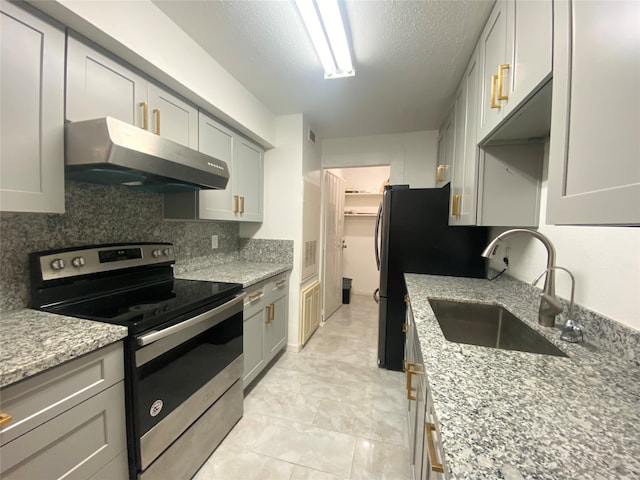 kitchen with electric range, light stone counters, sink, tasteful backsplash, and a textured ceiling