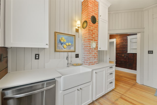 kitchen with white cabinets, wood walls, light hardwood / wood-style flooring, stainless steel dishwasher, and sink