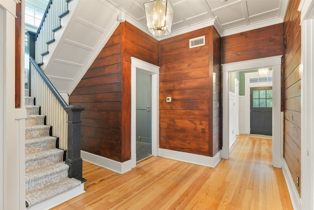 foyer entrance with a notable chandelier, coffered ceiling, light hardwood / wood-style flooring, wooden walls, and crown molding