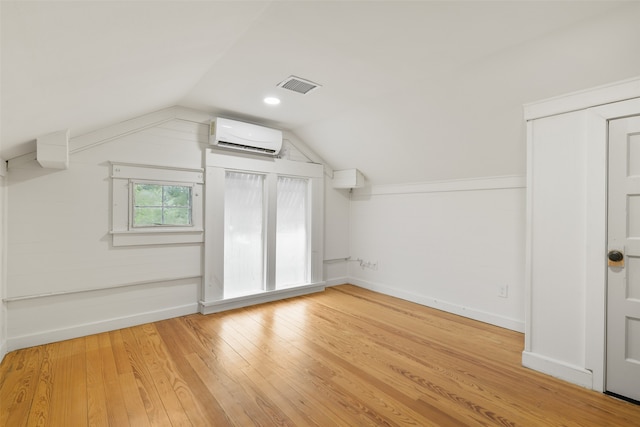 additional living space with light hardwood / wood-style flooring, lofted ceiling, and an AC wall unit