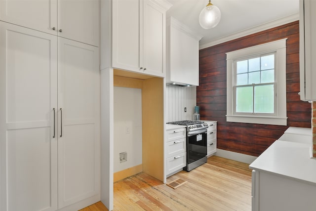 kitchen with light wood-type flooring, white cabinetry, stainless steel gas range oven, and wooden walls