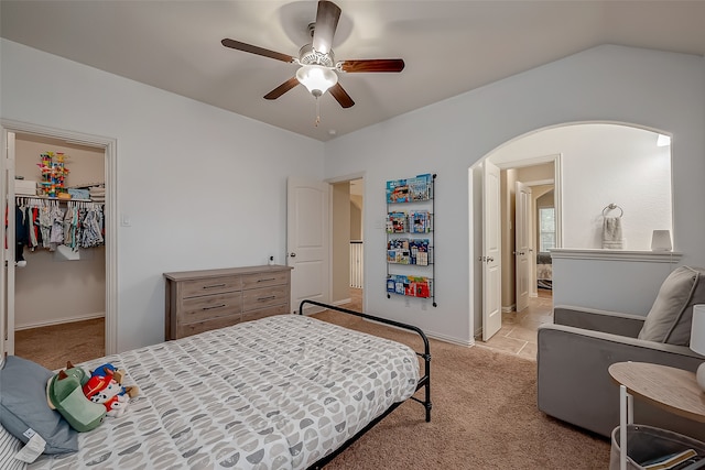 bedroom with a closet, a walk in closet, light colored carpet, and ceiling fan