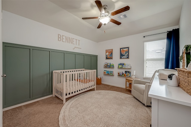 bedroom with ceiling fan, light colored carpet, and a crib