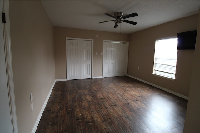 unfurnished bedroom with hardwood / wood-style floors, ceiling fan, a textured ceiling, and multiple closets