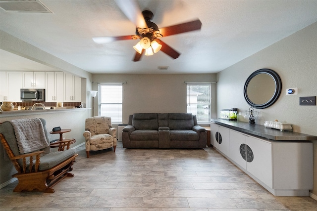 living room featuring ceiling fan, plenty of natural light, light hardwood / wood-style floors, and a textured ceiling