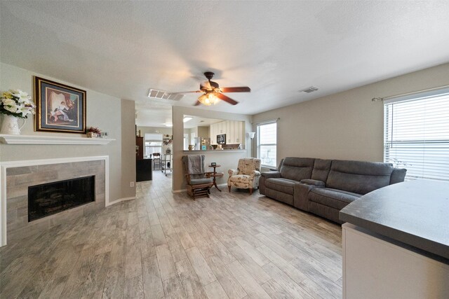 living room with ceiling fan, a tile fireplace, a textured ceiling, and light hardwood / wood-style flooring