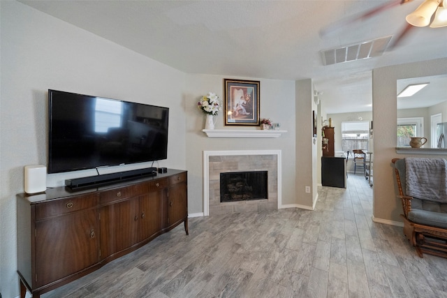 living room featuring ceiling fan, a tiled fireplace, and light wood-type flooring