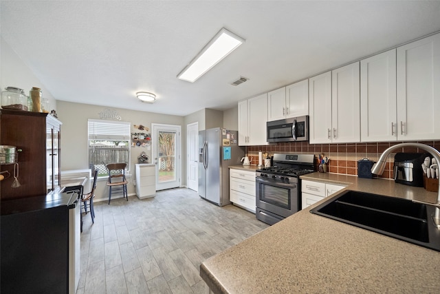 kitchen with light hardwood / wood-style flooring, stainless steel appliances, sink, decorative backsplash, and white cabinets