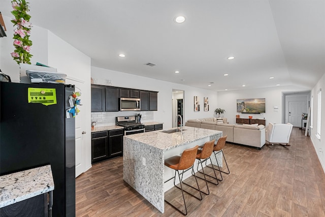 kitchen featuring a kitchen island with sink, a breakfast bar, stainless steel appliances, sink, and hardwood / wood-style flooring