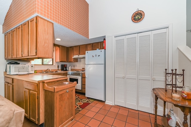 kitchen featuring a towering ceiling, light tile patterned floors, white appliances, and sink