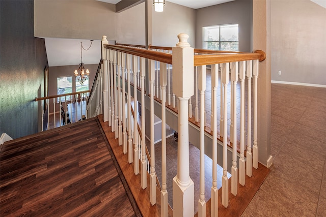 stairway with wood-type flooring, vaulted ceiling, an inviting chandelier, and a healthy amount of sunlight