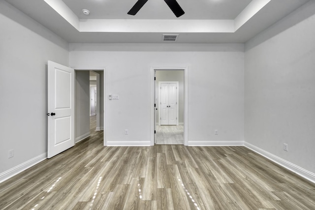 unfurnished bedroom with ceiling fan, a raised ceiling, and light hardwood / wood-style flooring